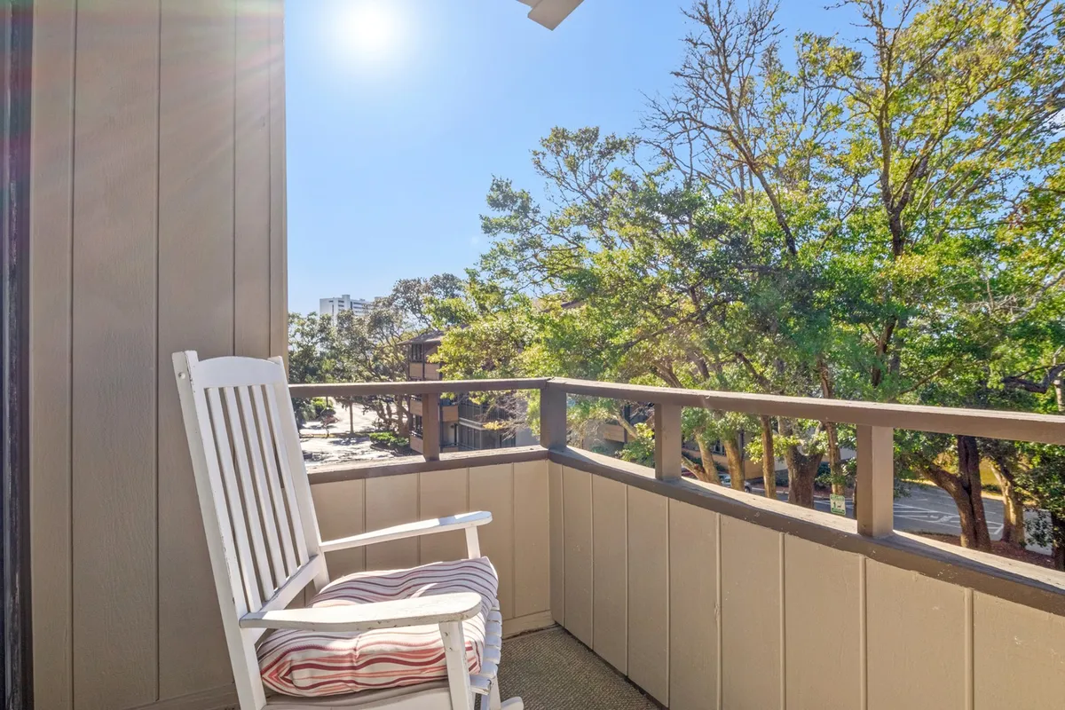 A tranquil view from an exterior balcony with a rocking chair and a sturdy railing, overlooking lush trees in the background. The space is perfect for sipping coffee, reading, or simply enjoying the peaceful ambiance of nature.