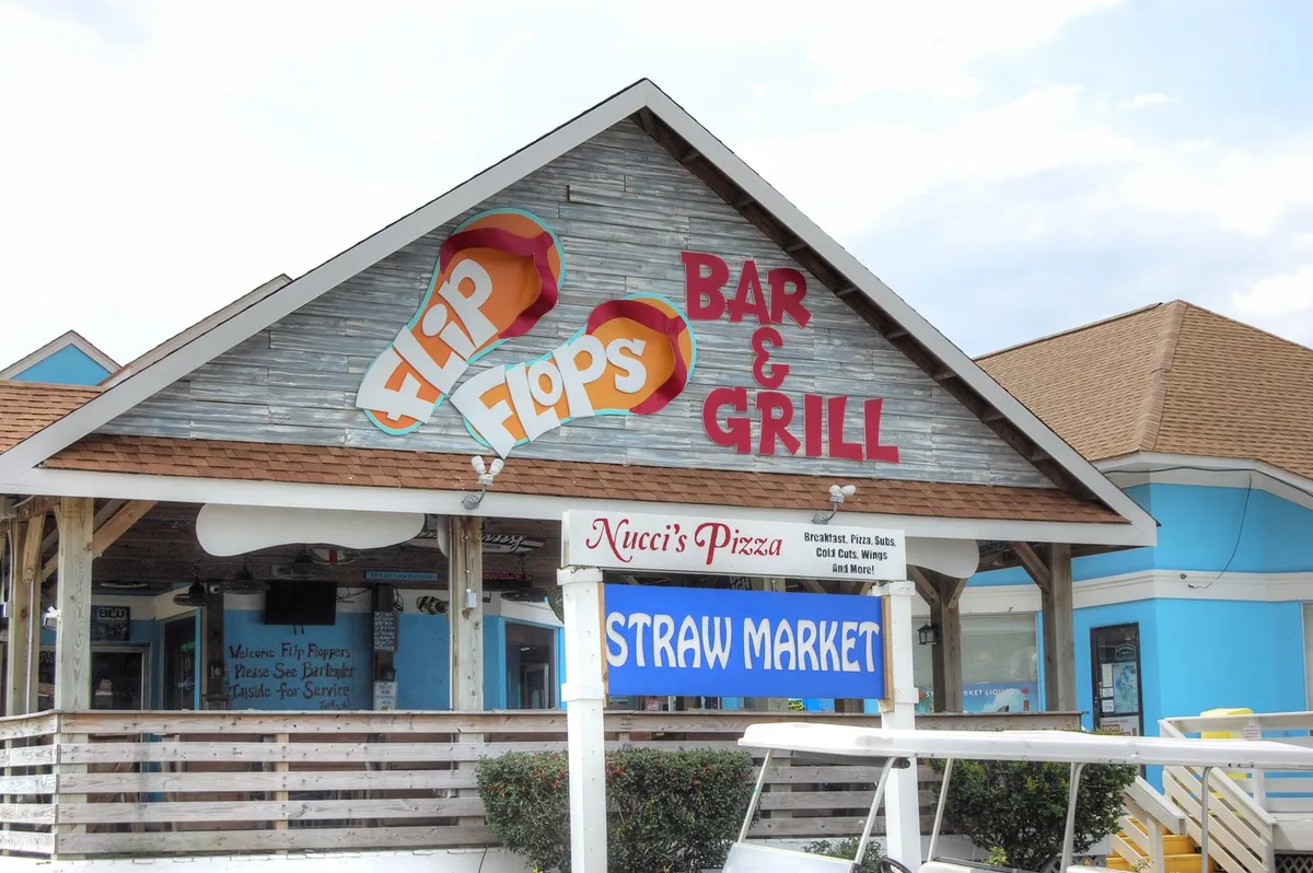 An exterior shot featuring the signs of Flip Flops Bar & Grill, Nucci’s Pizza, and Straw Market, hinting at vibrant dining and nightlife options within walking distance of Mariners Cove.