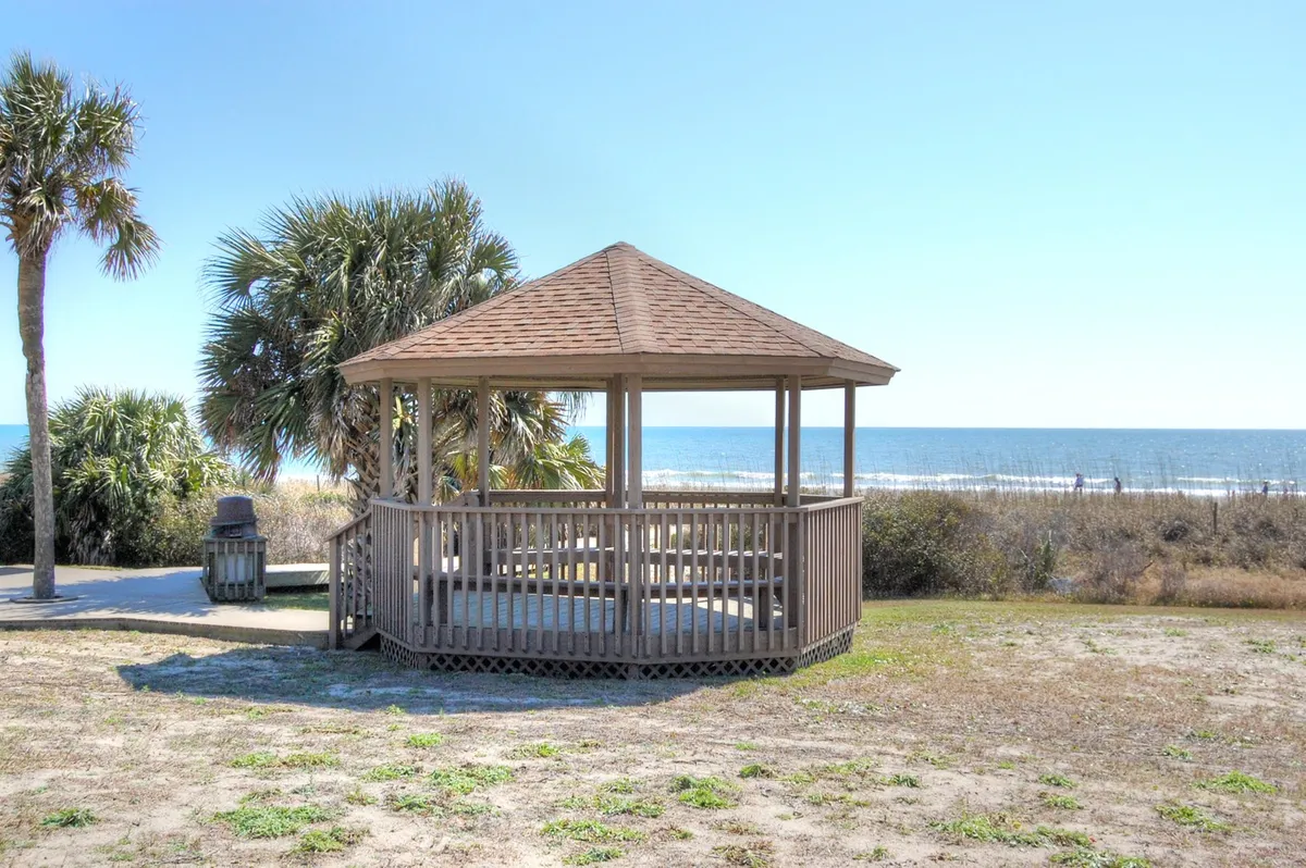 A tranquil scene with a gazebo facing the ocean, framed by palm trees. The seating area under the gazebo invites quiet moments, with the ocean stretching out in the background.