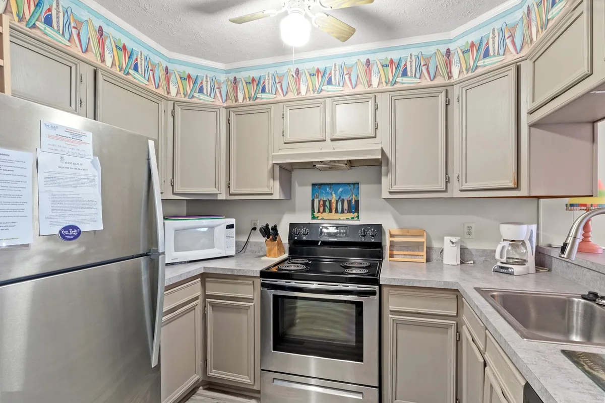 This image showcases a kitchen with a stainless steel refrigerator, a black stove, a colorful backsplash, and a wooden utensil holder on the counter. The scene feels bright and lively, with ample workspace and visible cookware.