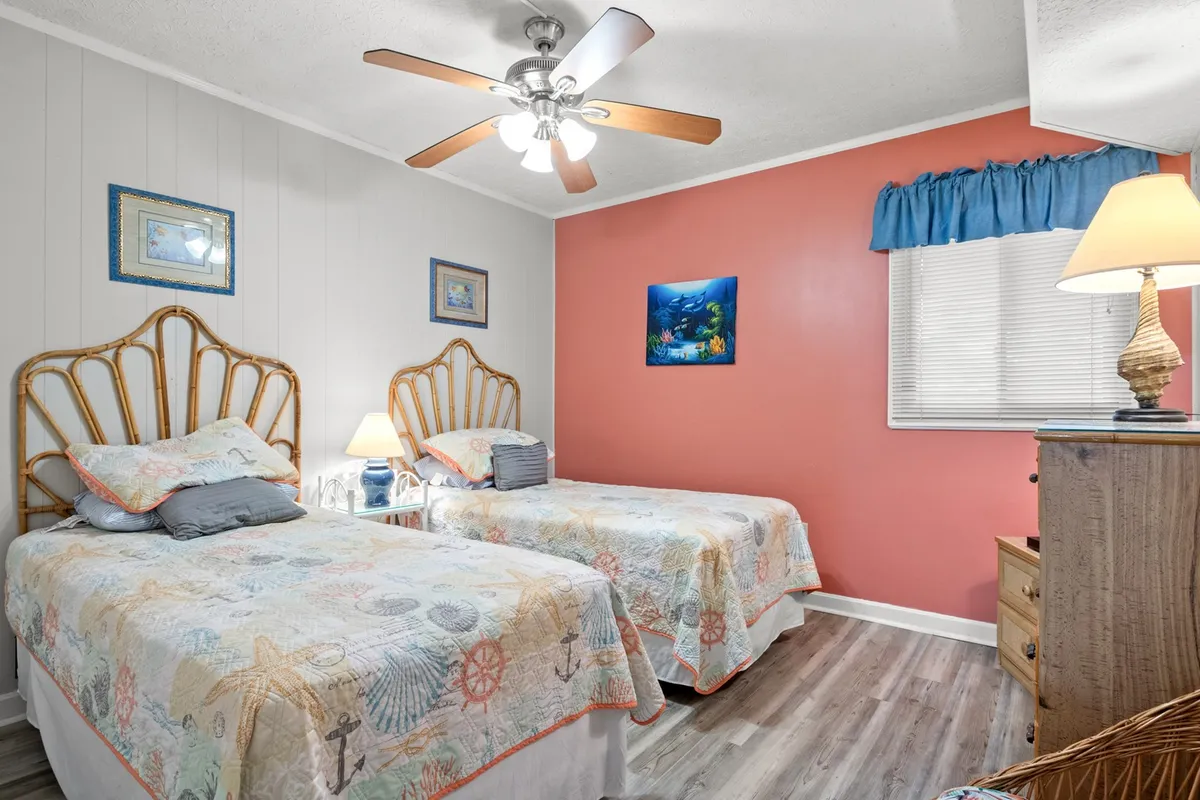 This image shows two twin beds with ocean-themed bedspreads, a ceiling fan for added comfort, and colorful wall art that creates a playful, family-friendly atmosphere. The room feels bright and cheerful, ideal for children or friends sharing the space.