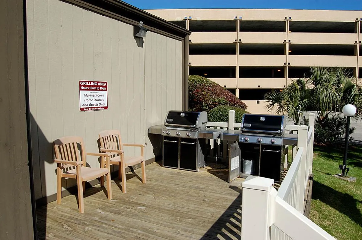 A relaxed outdoor grilling area with wooden chairs and lush greenery, ideal for group barbecues, casual gatherings, and social evenings under the open sky. The setup exudes a friendly, welcoming mood, inviting guests to create shared memories.
