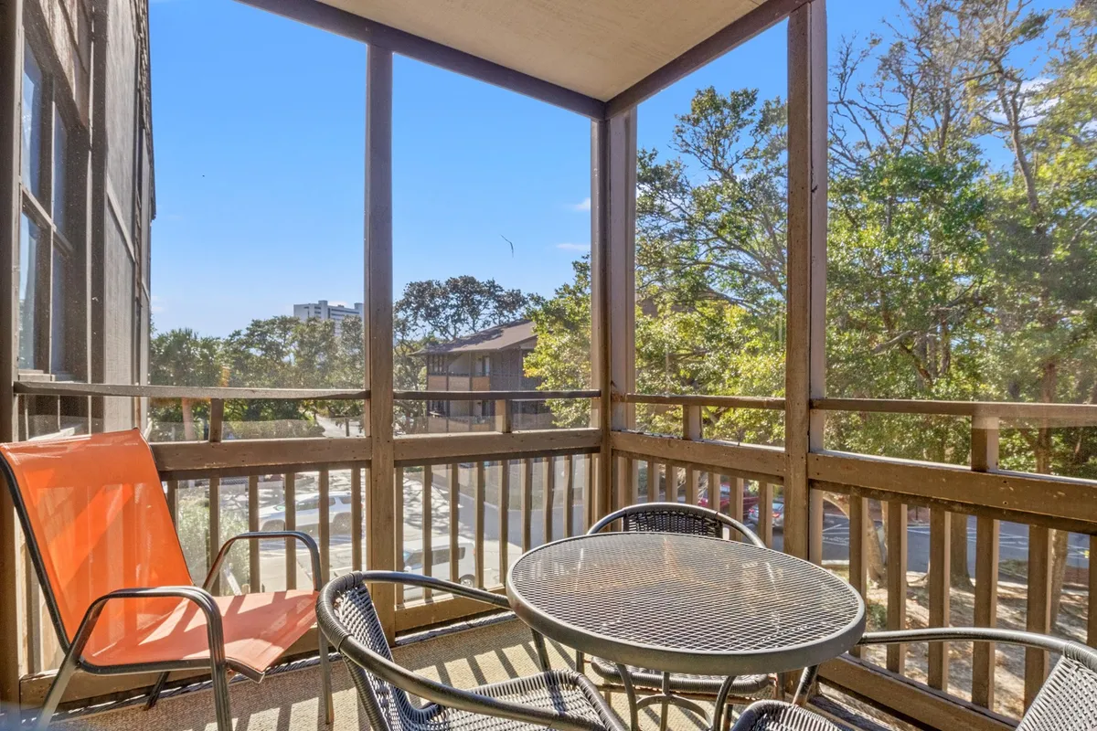 A cozy interior scene featuring an orange chair and a metal table, positioned on a screened balcony with views of greenery outside. The setting is inviting, designed for enjoying a quiet morning coffee, afternoon reading, or evening relaxation while protected from the elements.