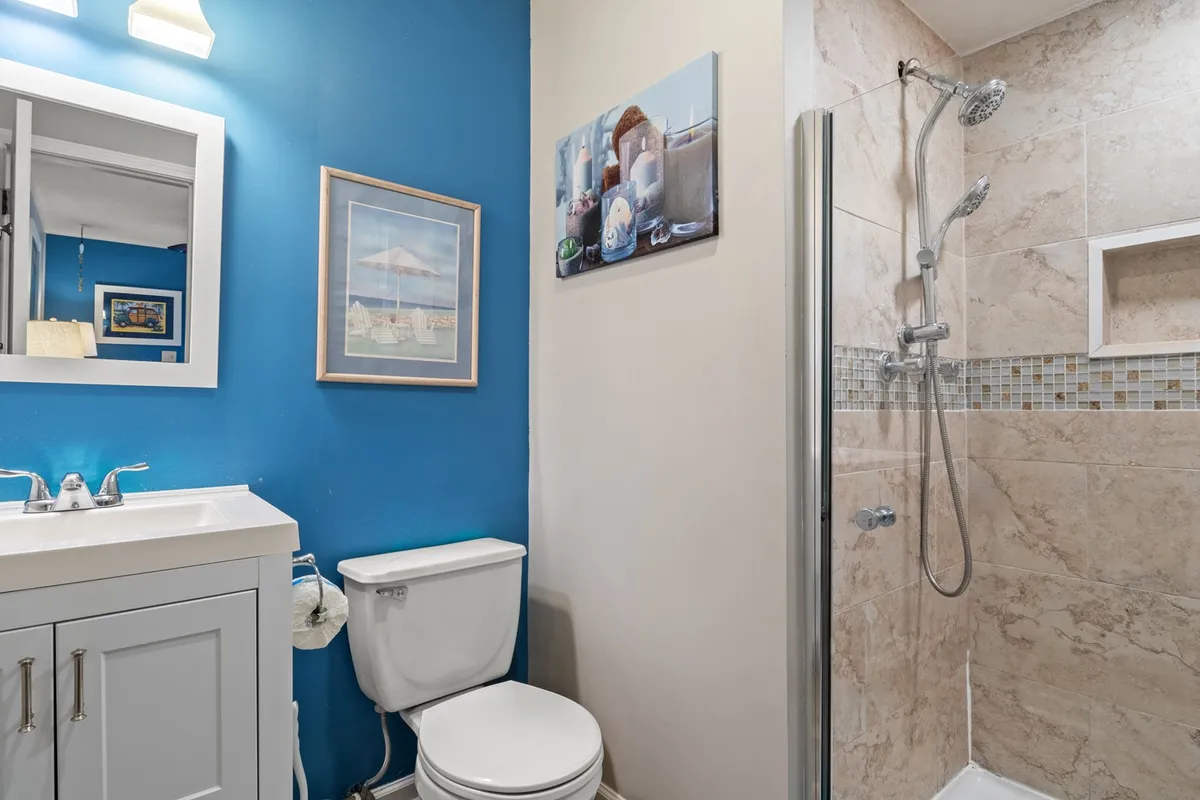 A modern bathroom with a blue accent wall, sleek shower, white vanity, and tasteful wall art. The space feels clean, fresh, and rejuvenating—ideal for starting the day or winding down in the evening.